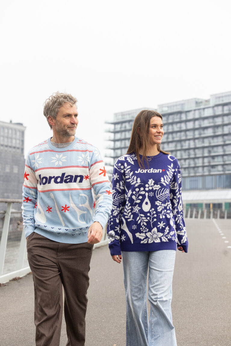 2 modellen lopend over straat in bedrukte kersttruien. 1tje in het licht en de andere in het donker blauw.